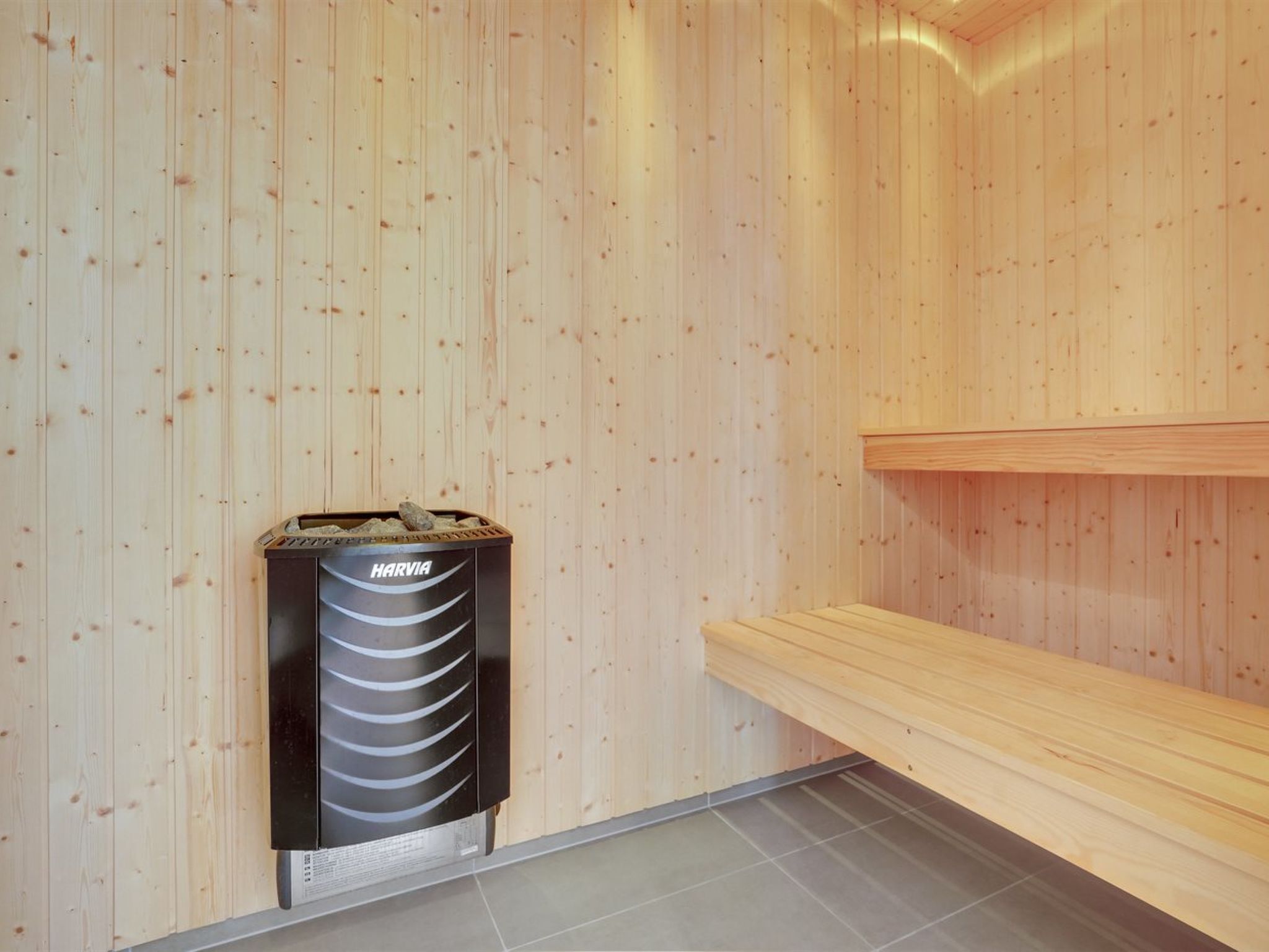 Una sauna con pareti in legno, una sauna Harvia e una panca di legno.