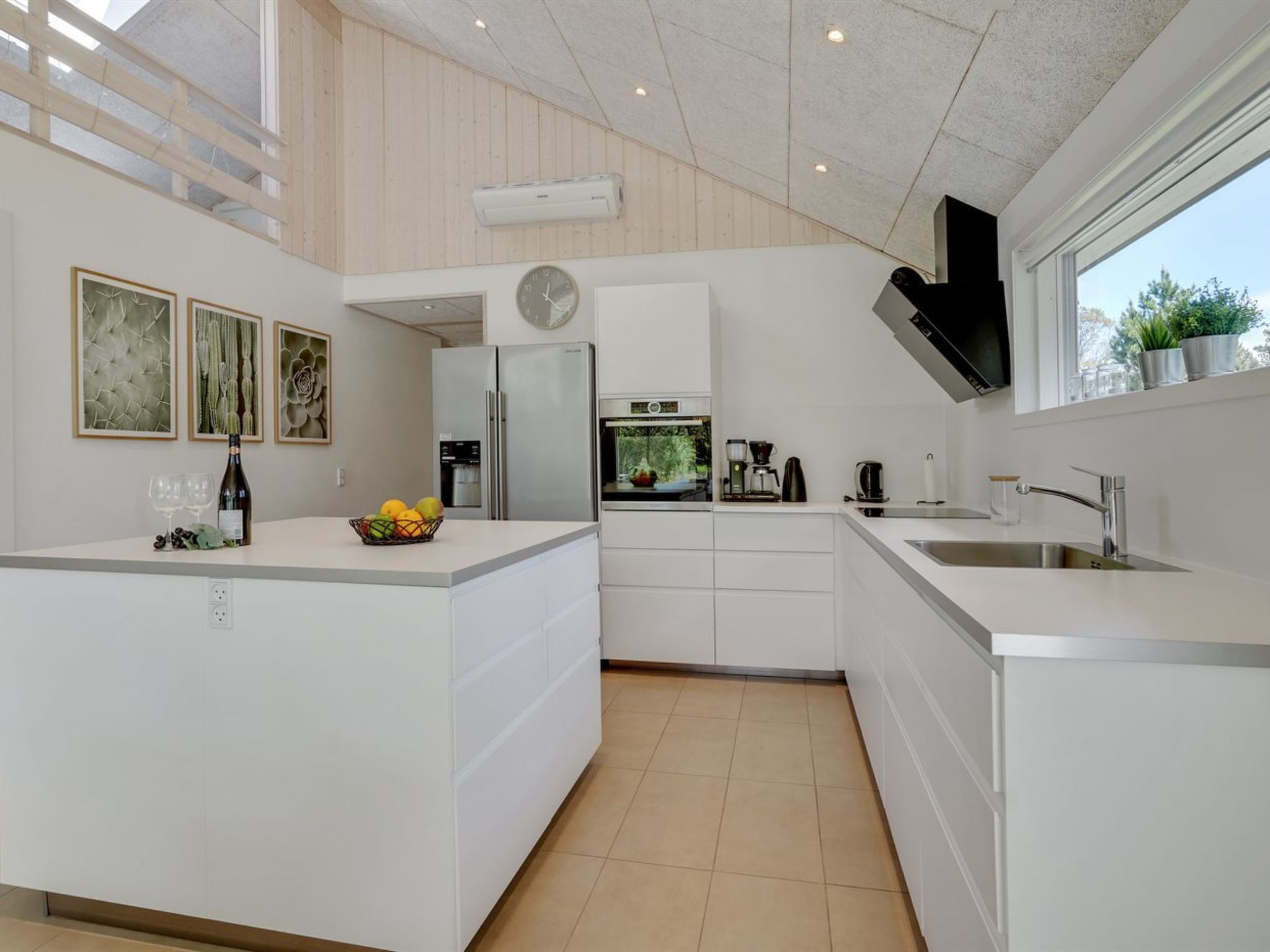 Een moderne keuken met witte kasten, een inbouwoven, een koffiezetapparaat en een groot raam.