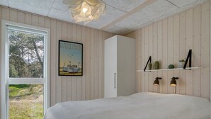 A bedroom with a large bed, a window with a view of trees, a framed picture of a boat, and a shelf with plants. - "Delan" - 1.3km from the sea by Interhome (Vejers Strand)