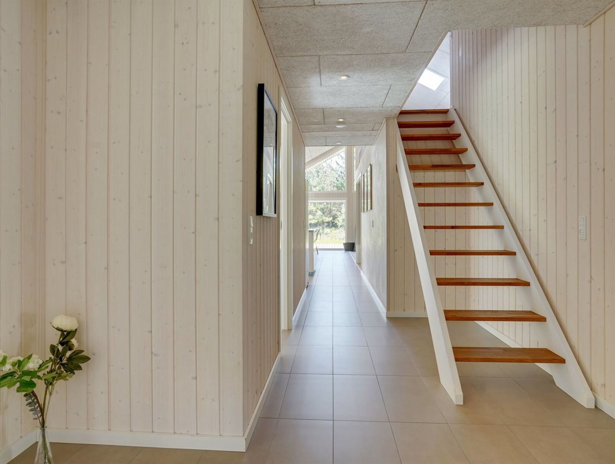 A hallway with wooden panel walls, a tiled floor, and a wooden staircase.