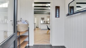 A hallway with a wooden floor, a black-framed mirror, and a woven basket on a metal shelf.