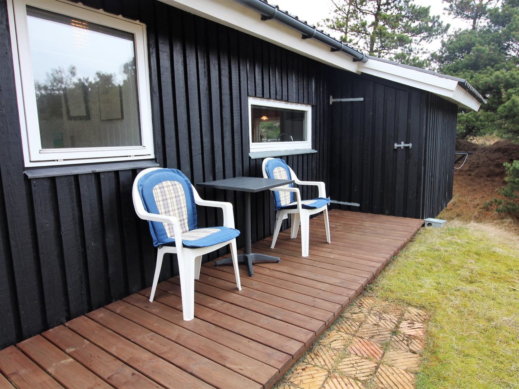 A black building with a wooden deck, two white chairs with blue cushions, and a table.