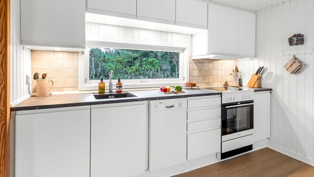 Una cocina moderna con armarios blancos, encimera negra, lavavajillas Bosch y horno.