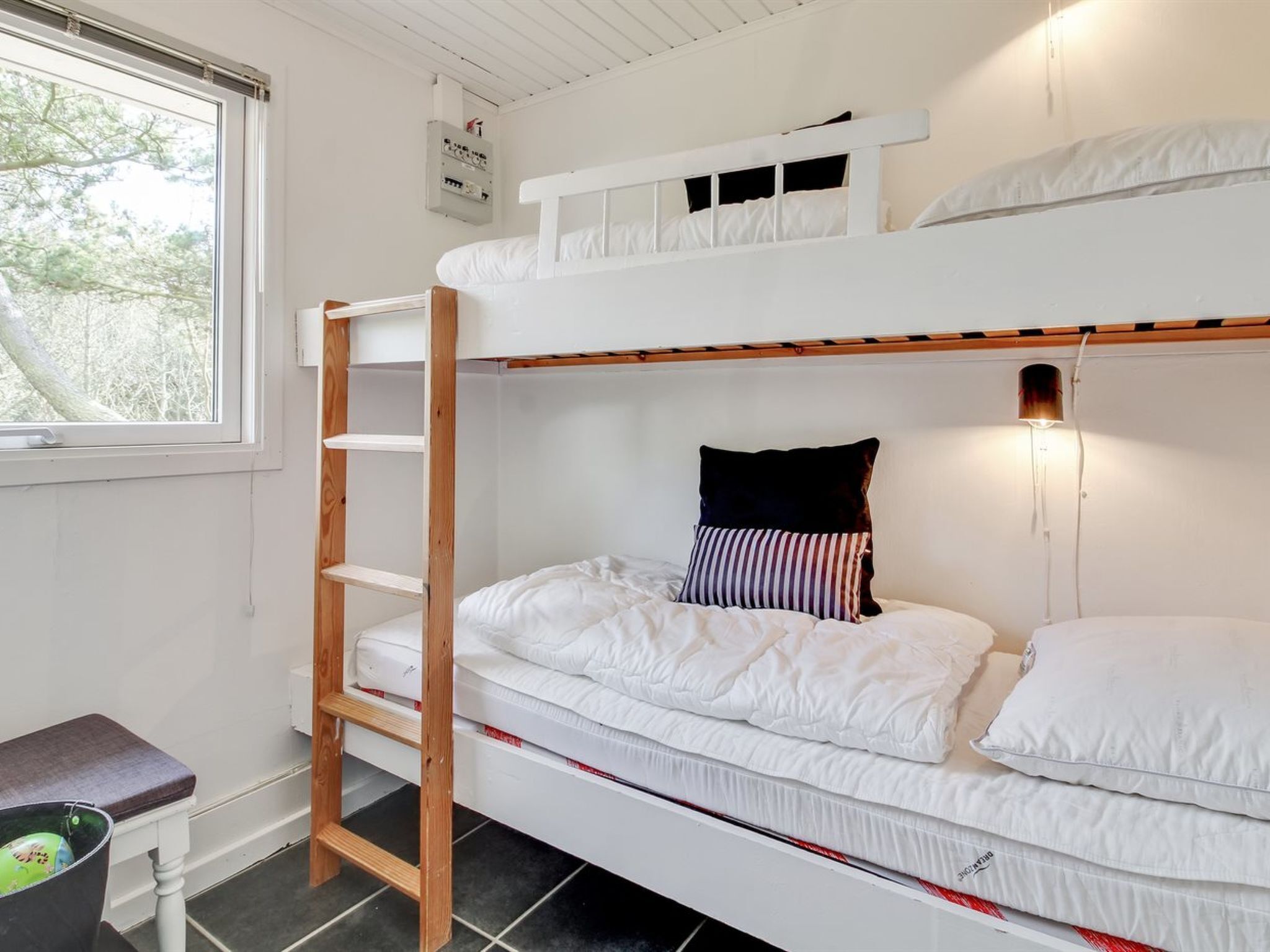 Une chambre avec un lit superposé, une petite échelle, une petite table et une poubelle.