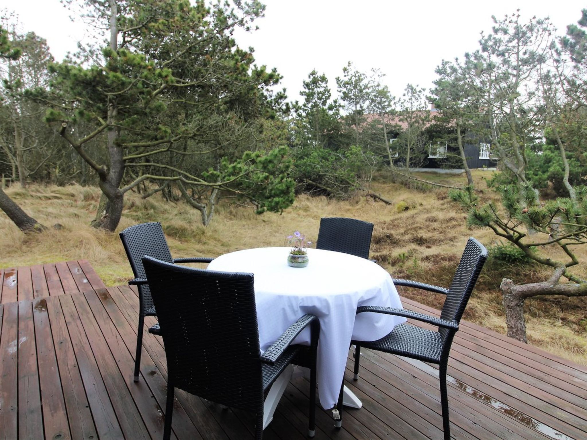 An outdoor dining area with a round table and four chairs, surrounded by trees and a wooden deck.