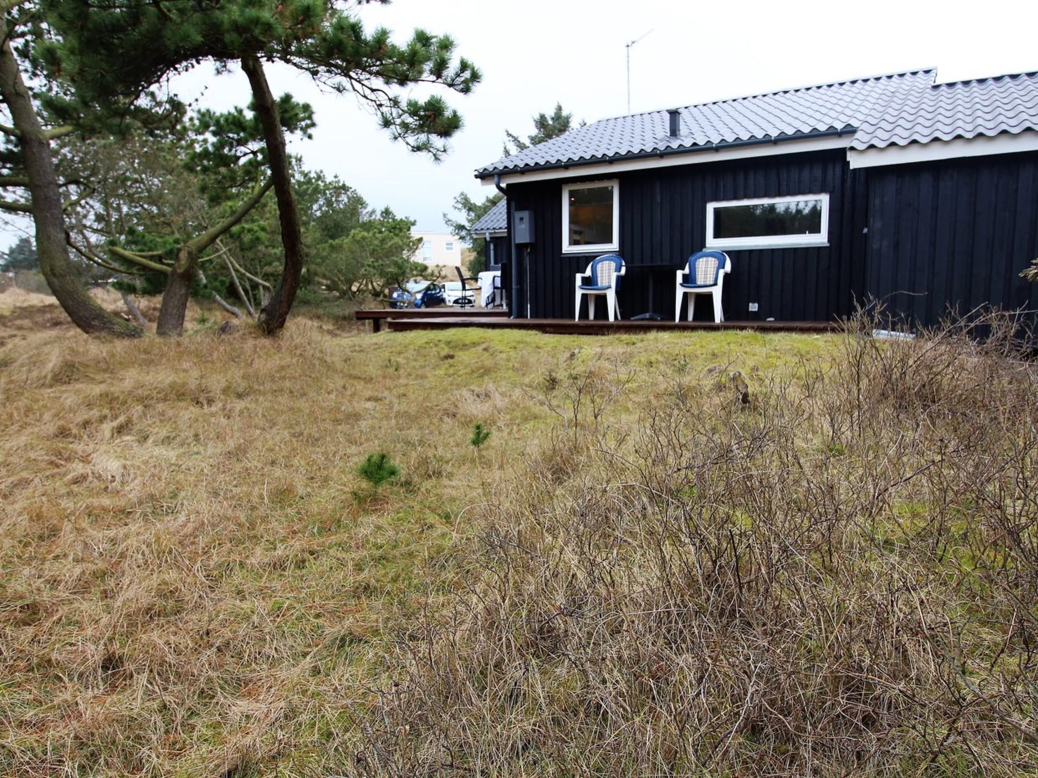 A black building with a metal roof, two windows, and a small deck with two chairs.