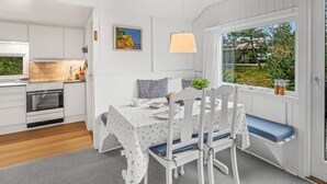 Una cocina moderna con armarios blancos, horno empotrado y un comedor con mesa y sillas.