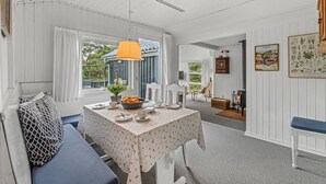 Una habitación acogedora con techo de madera blanca, una mesa de comedor con mantel floreado, un banco azul y una lámpara naranja colgante.