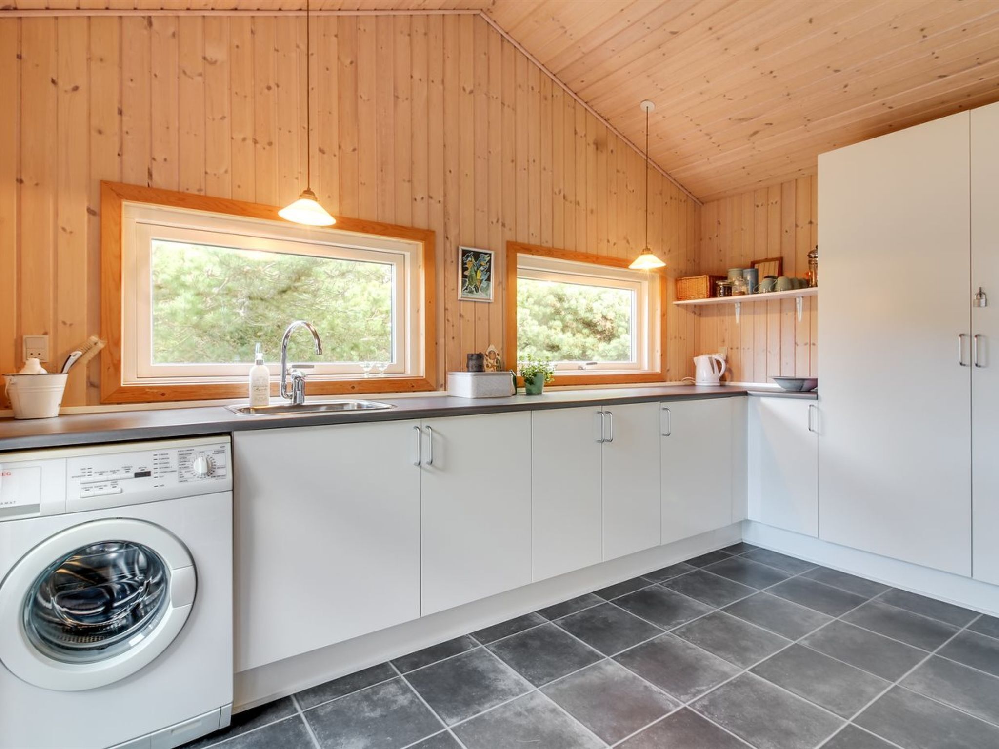 Eine moderne Küche mit Holzwänden, zwei Fenstern, einer Waschmaschine und einem Spülbecken.