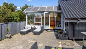Ein modernes Haus mit einer Terrasse, die Gartenmöbel und einen gläsernen Anbau umfasst.