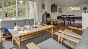 A cozy living room with a fireplace, a dining area, and large windows offering a view of the outdoors.