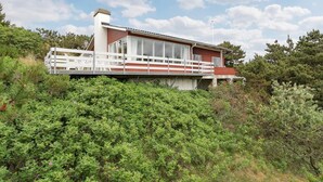 A modern house with a red and white exterior, a balcony, and surrounded by dense greenery.