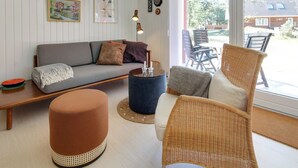A cozy living room with a sofa, ottoman, and wicker chair, a coffee table, and a bookshelf with books and decorative items. - "Aulikki" - 900m from the sea by Interhome (Vejers Strand)