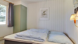 A neatly made bed with a mattress and pillows, a window with curtains, a wall-mounted lamp, and a framed picture on the wall. - "Aulikki" - 900m from the sea by Interhome (Vejers Strand)