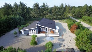 A modern house with a large deck, surrounded by dense forest.