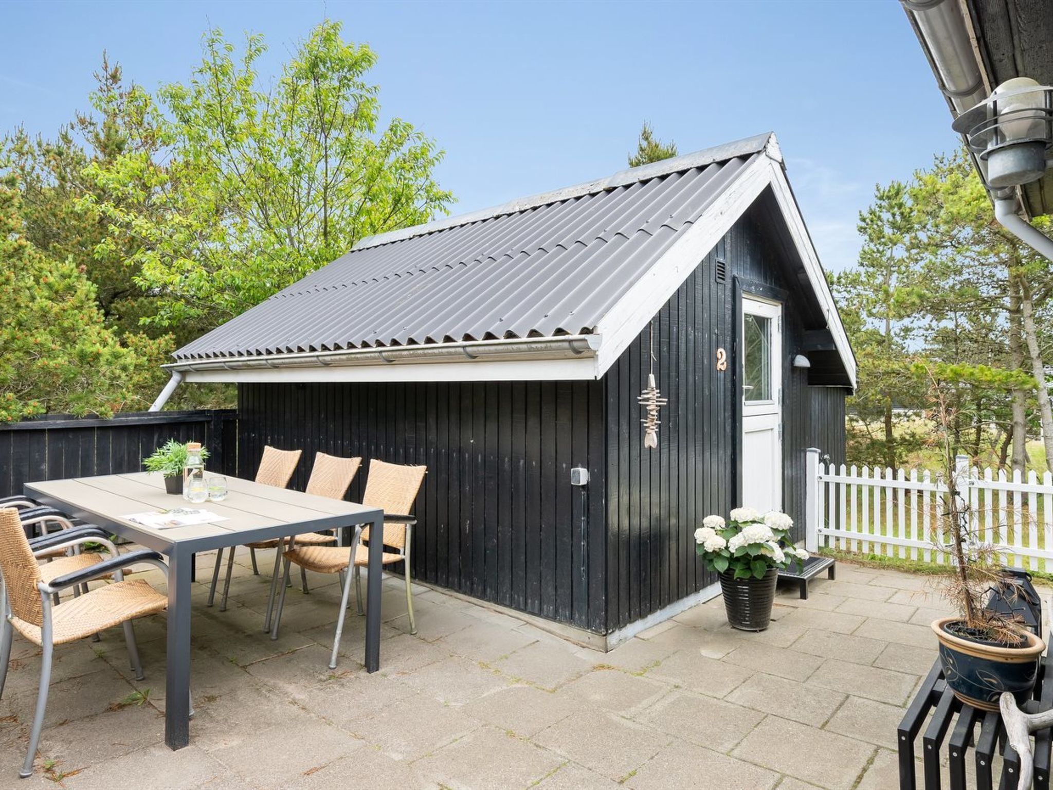 En sort træbygning med skråtag, en hvid dør og en lille veranda med et bord og stole.