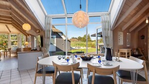 A dining area with a large table, chairs, and a view through large windows.