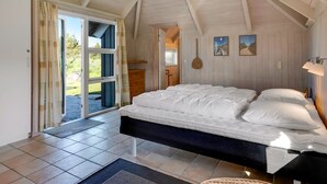 A bedroom with a bed, a door leading outside, and a ceiling with wooden beams.