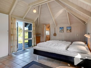 A bedroom with a bed, a door leading outside, and a ceiling with wooden beams.