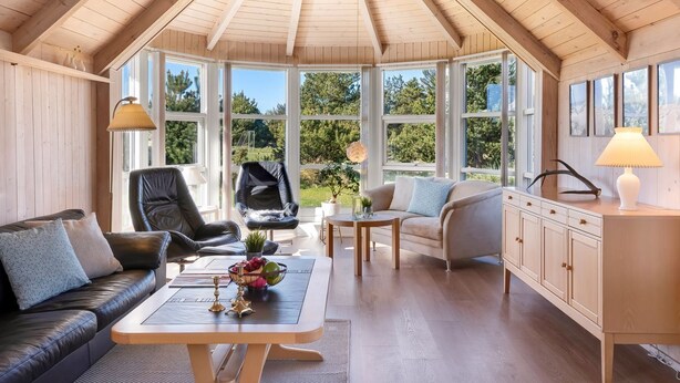 A spacious room with a sloped ceiling, large windows, a sofa, a chair, a table with a vase, and a cabinet.