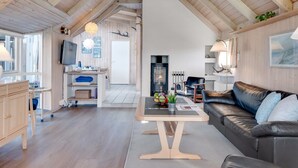 A modern interior with a wooden ceiling, a living area with a sofa and coffee table, a kitchen with a TV, and a fireplace.