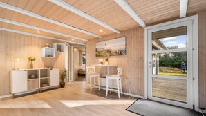 Un interior moderno con pisos de madera, mobiliario blanco, un comedor y un amplio ventanal con vistas al exterior.