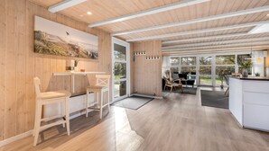 Cocina moderna con paredes y techo de madera, comedor con sillas y un amplio ventanal con vistas al exterior.