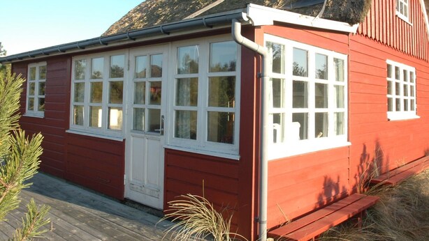 Un bâtiment en bois rouge, avec des fenêtres à cadre blanc et un toit de chaume.