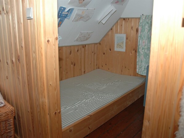 A small, wooden room with a single bed, a sloped ceiling, and a wall adorned with children's drawings.