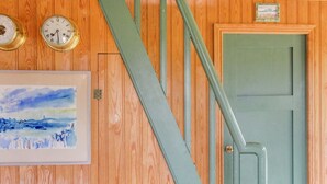 Un intérieur en bois avec une porte verte, un escalier et deux horloges fixées au mur.