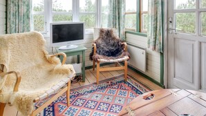 Une pièce confortable avec une grande fenêtre, un bureau avec un ordinateur, un fauteuil recouvert de fourrure et une table en bois.