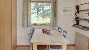 Un'area pranzo con un tavolo di legno, sedie, una finestra con tende, una lampada a sospensione e una mensola a muro con stoviglie.