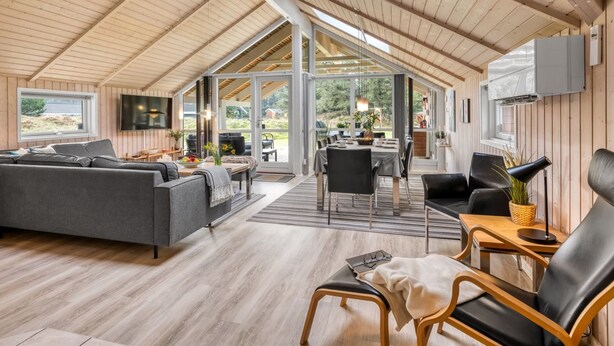 Um amplo quarto no estilo loft com teto alto, vigas de madeira, uma grande mesa de jantar e um espaço de estar aconchegante com sofá e poltronas.