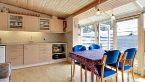 A modern kitchen with wooden cabinets, a dining area with blue chairs, and a large window offering a view of the outside. - "Genadij" - 1km from the sea by Interhome (Vejers Strand)