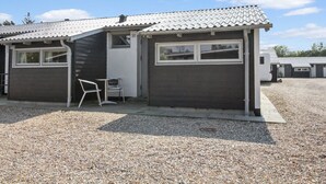 A single-story building with a tiled roof, two garage doors, and a small outdoor seating area with a metal chair and table. - "Genadij" - 1km from the sea by Interhome (Vejers Strand)