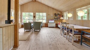 Un interior de cabaña acogedor, con revestimiento de madera, una chimenea, una zona de comedor y ventanas amplias.