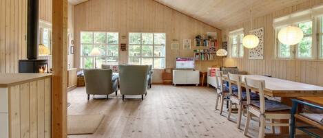 A cozy cabin interior with a wooden interior, a fireplace, a dining area, and large windows.