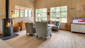 Una habitación acogedora con una estufa de leña, un sofá, un televisor y ventanas amplias.