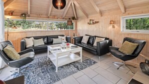 A spacious living room with a high ceiling, wooden walls, and large windows offering a view of greenery outside. - "Kenny" - 1.2km from the sea by Interhome (Vejers Strand)