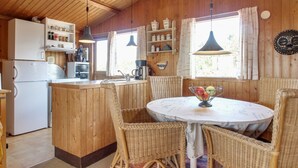 Ein Holzinnenraum mit Küchenbereich, Korbstühlen, einem runden Tisch und einem Kühlschrank.