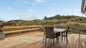 Eine Holzterrasse mit Tisch und Stühlen mit Blick auf einen grasbewachsenen Hügel.