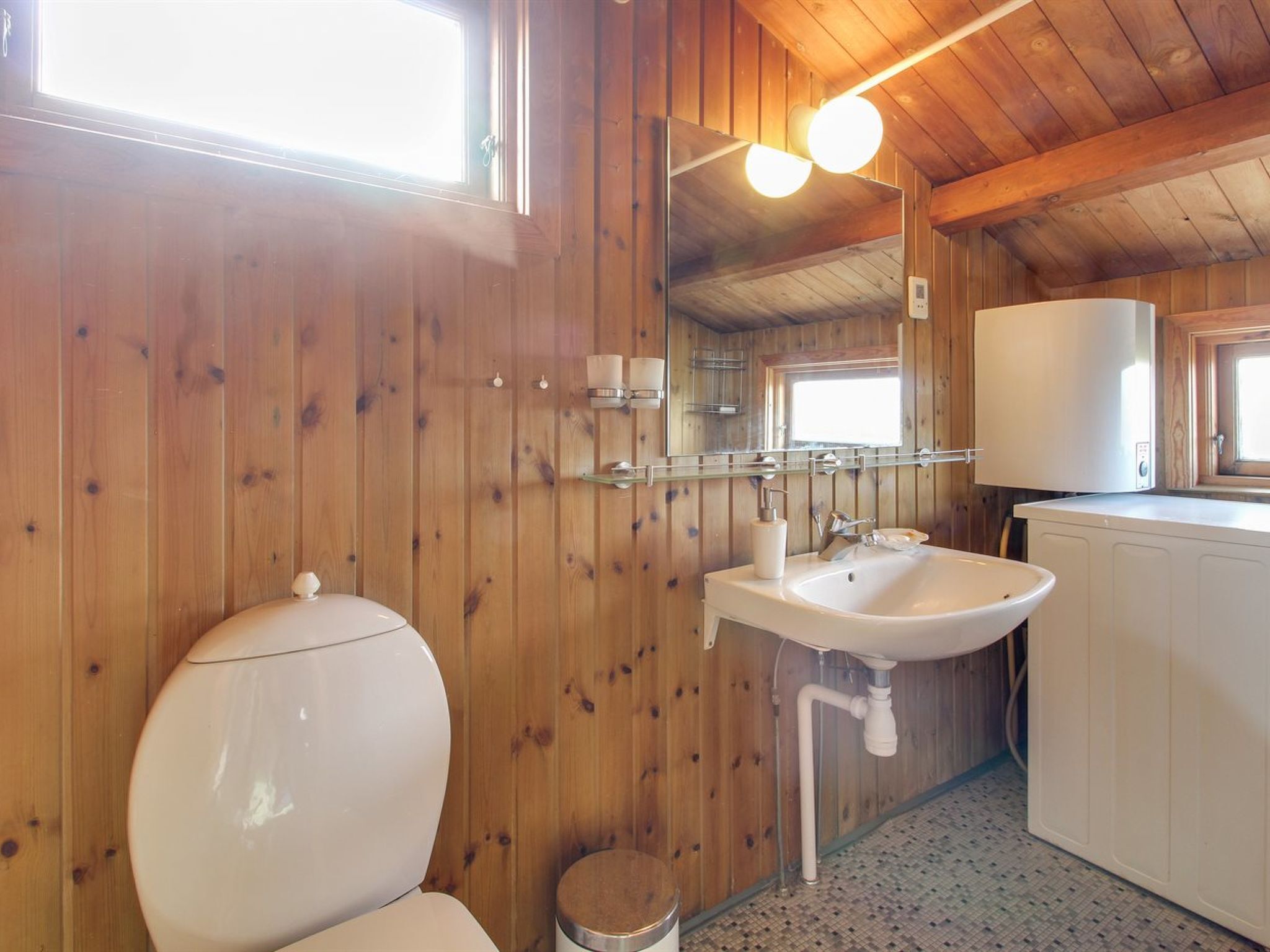 A wooden cabin bathroom with a toilet, sink, and mirror.