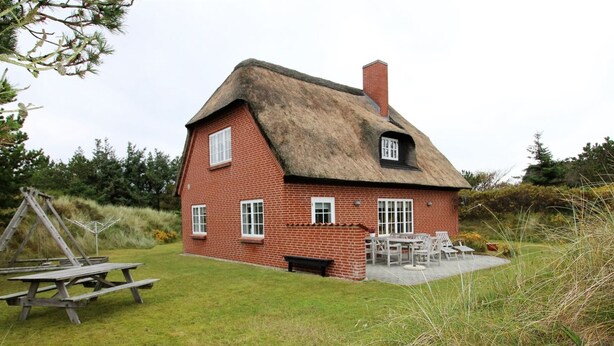 A red brick house with a thatched roof, a patio with outdoor furniture, and a swing set in the yard. - "Lioba" - 400m from the sea by Interhome (Vejers Strand)