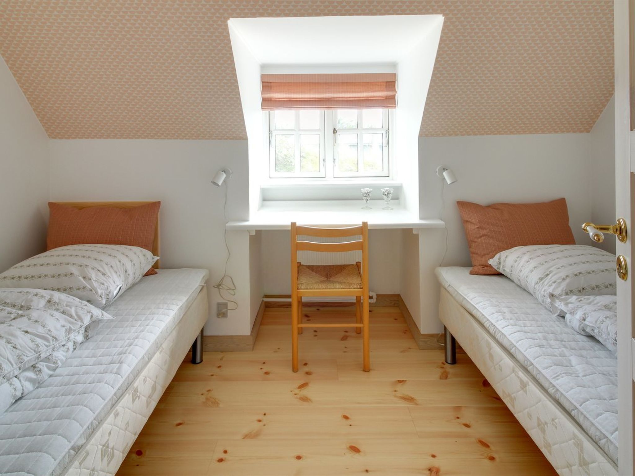 A dormitory room with two single beds, a wooden desk, and a window with a view.