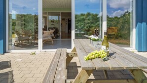 Une maison moderne dotée d’un patio comprenant une table en bois, une bouteille de vin, un verre et une grappe de raisins.