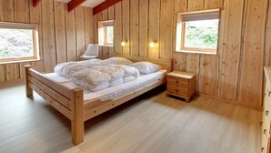 Camera da letto in una baita di legno, con un letto, comodini e finestre.