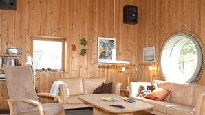 Una stanza accogliente con arredamento in legno, uno specchio rotondo, un divano, una poltrona e un tavolino con una lampada.