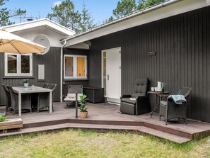 A modern outdoor patio with a wooden deck, a table, chairs, and a covered area.