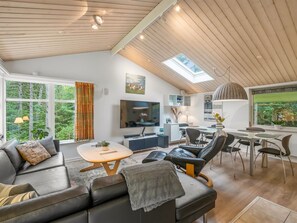 A modern living room with a sofa, a coffee table, a TV, and a dining area with chairs and a table.