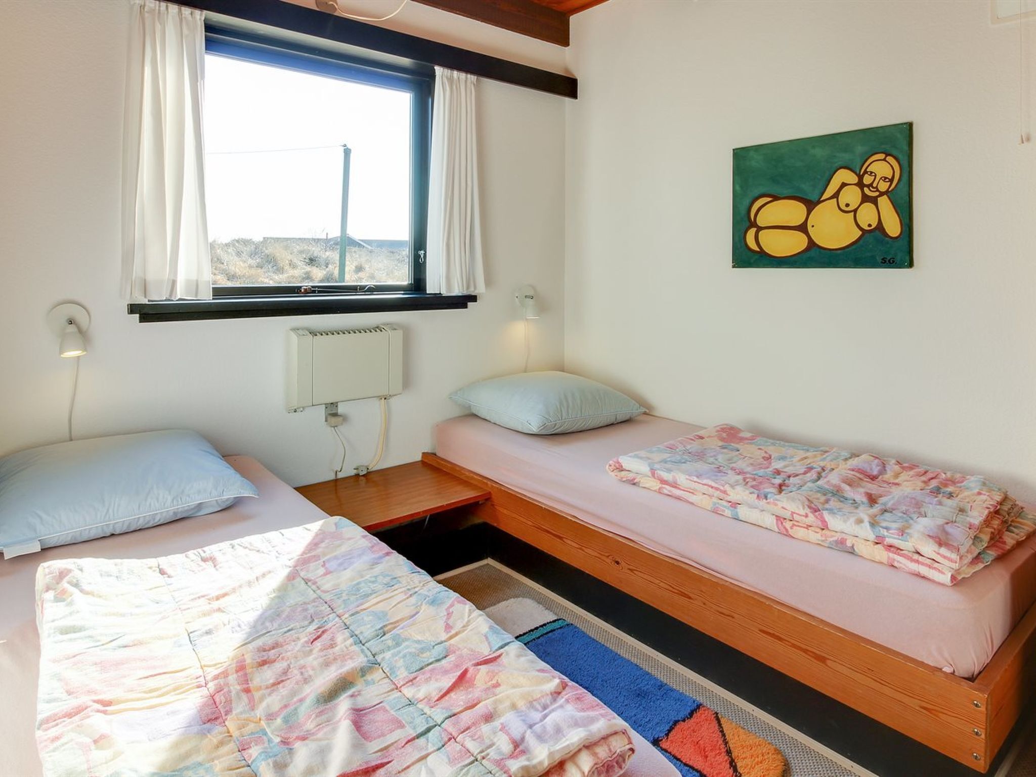 A room with two single beds, a window with curtains, a radiator, and a painting on the wall.